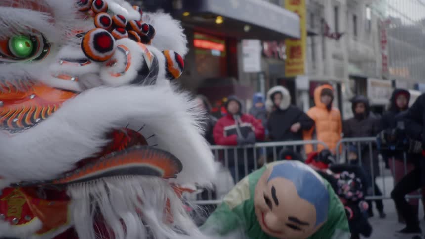 People in chinese parade costumes perform a dance for a crowd of people in a city