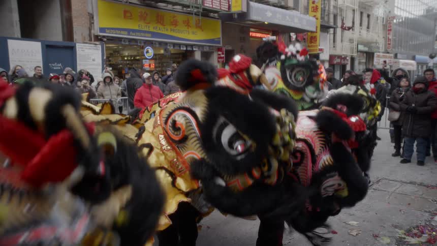 Performers dressed in chinese dragon costumes dance in the street in front of a crowd