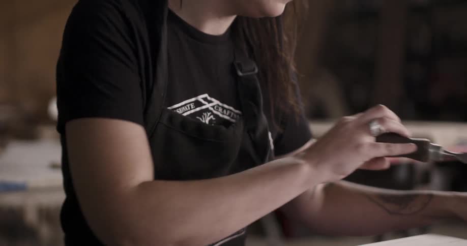 Woman with tattoo on her arm scratches a small piece of wood with screwdriver indoors during daylight