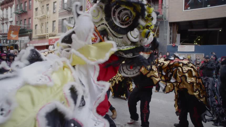 A group of people in chinatown performing lion dances in the street for a crowd