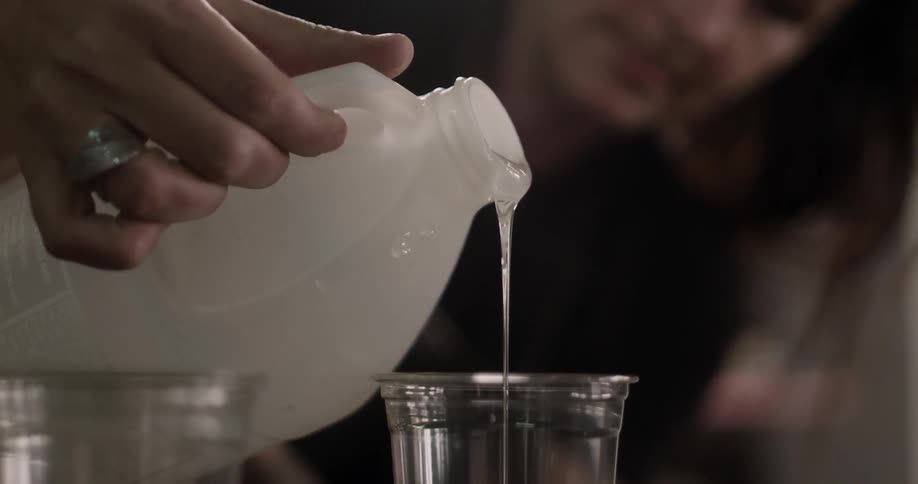 Clear liquid being poured from a white jug into a clear plastic cup