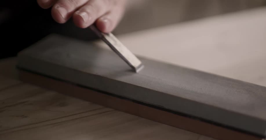 A metal tool is scraped across a wood board in a workshop