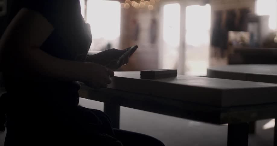 A person sits down at a workbench where they hold a chisel and angle the tip of its blade towards a small block of wood