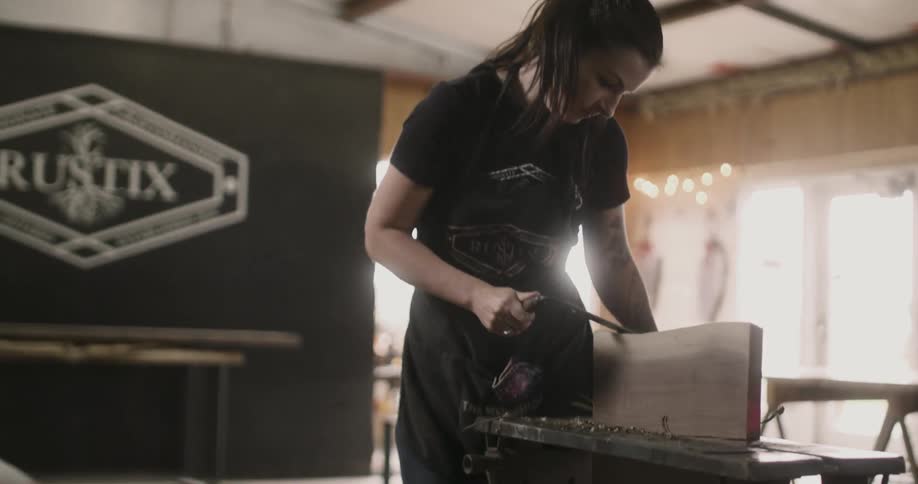 Young woman works on a piece of wood with a tool
