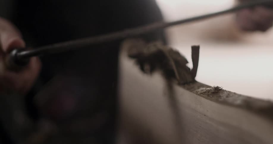 A woodworker uses a draw knife to shave a pieces of lumber