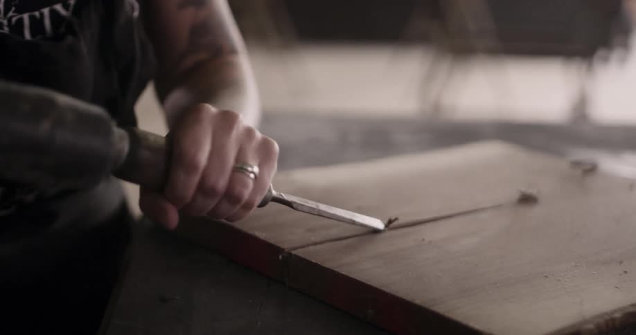 A carpenter chisels a groove into a piece of wood