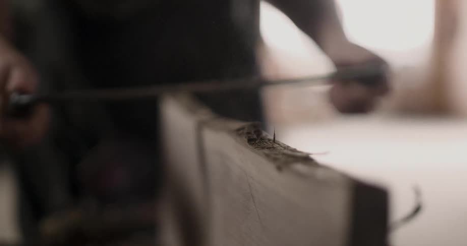 A person scrapes wood off the top of a plank