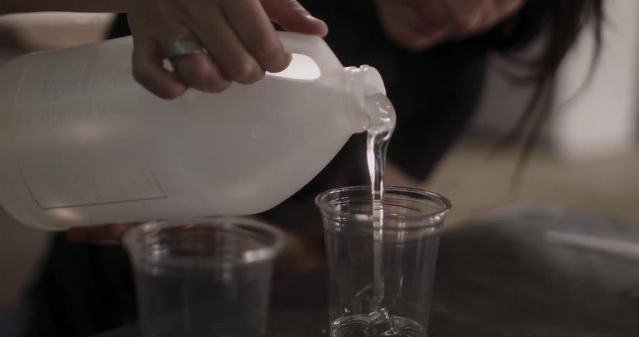 A person pouring a clear thick oil into a plastic cup