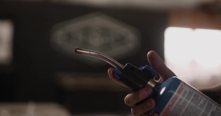 A person is turning the knob on a blue torch and then presses the button to ignite the flame