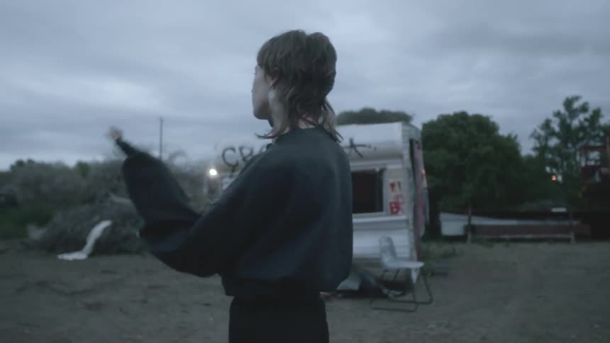 A female talks on a cell phone in a rural area in front of a broken down trailer and graffiticovered wall