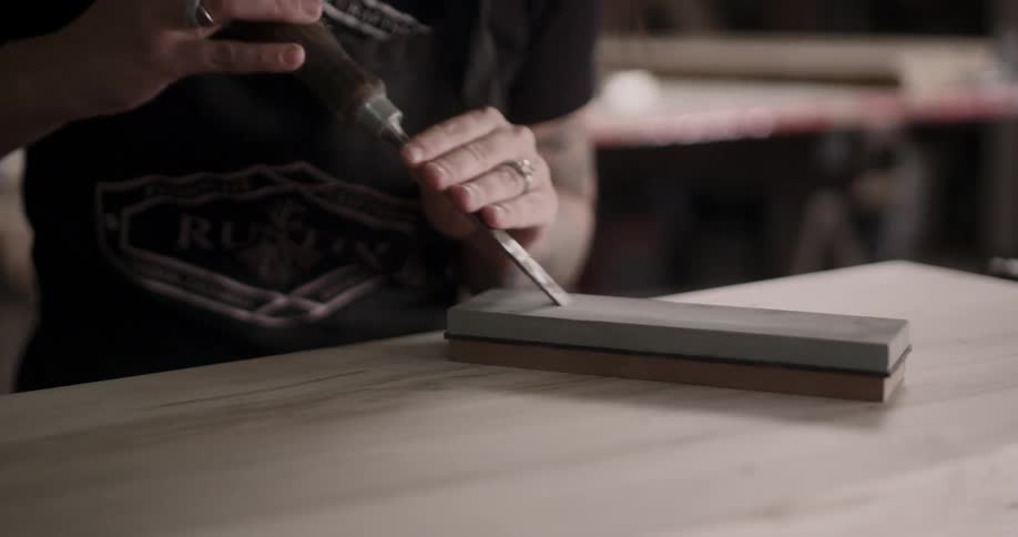 A woman sharpens a chisel on a soapstone