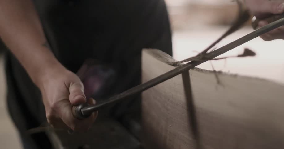 A man is shaving wood with a saw indoors