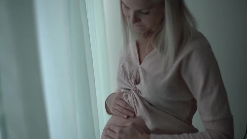 A woman rubs her hands across her pregnant stomach