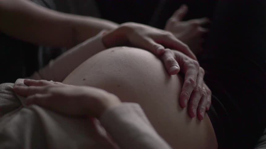A man and woman hold hands on top of a pregnant stomach while the baby kicks