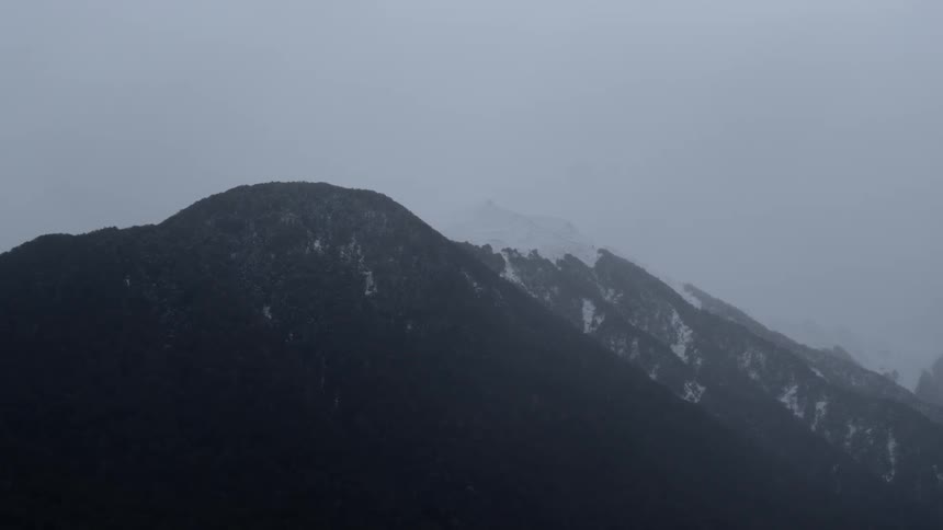 A partially snow capped rocky mountain range under a cloudy sky