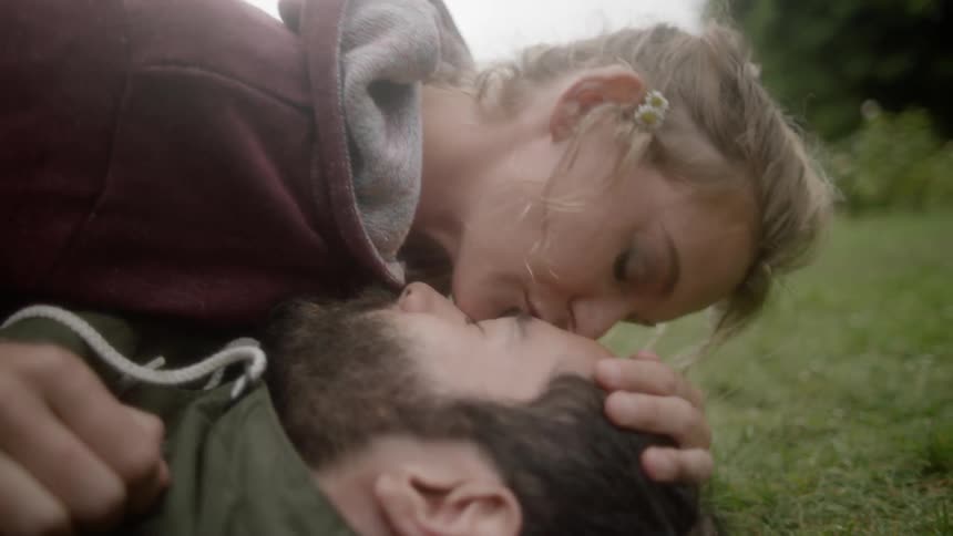 A woman kissing a man that is laying outside