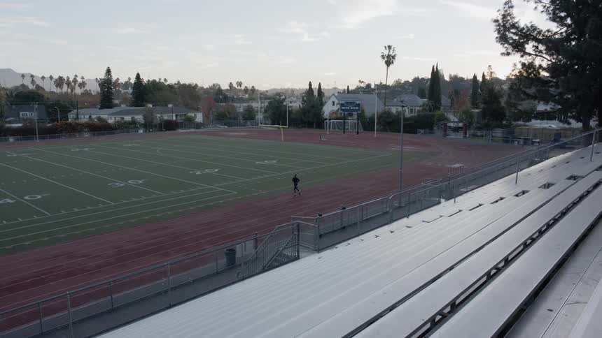 A jogger running along a track surrounding a football field