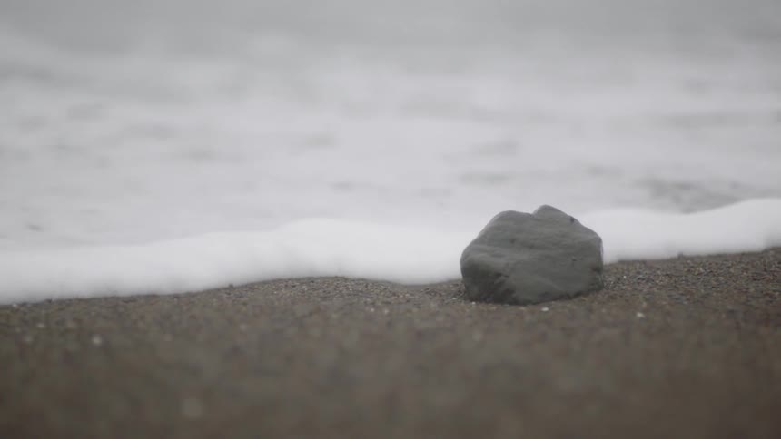 Waves come up and cover a small rock sitting on the beach