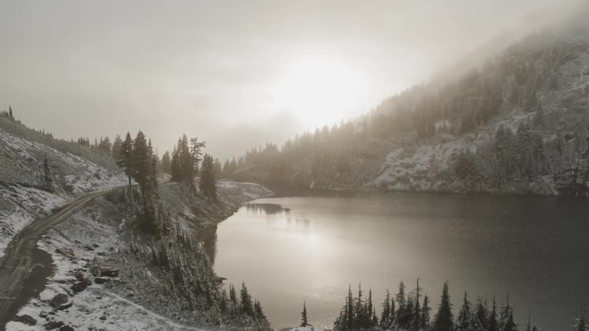 A lake and hills with snow falling