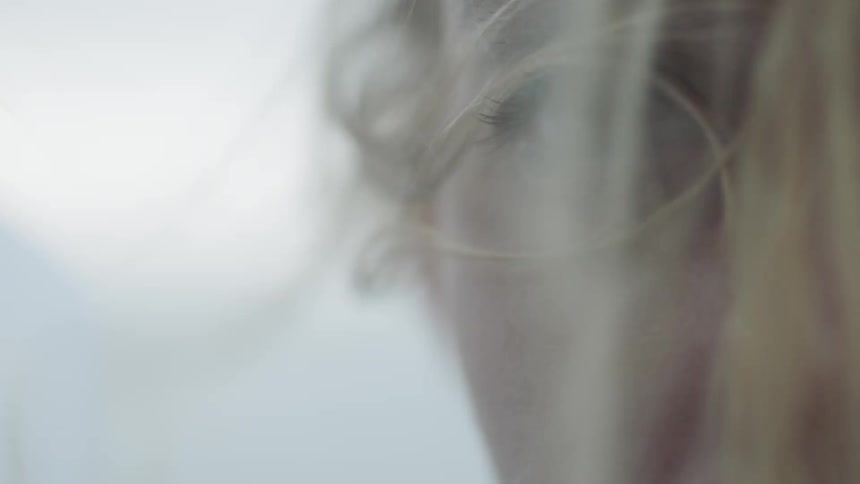 A closeup of a womans eyes as she is looking despaired and the breeze blows her hair around