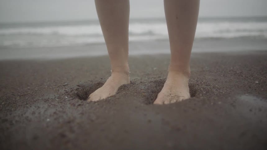 Woman presses with bare feeton beach sand next to the sea on a cloudy day