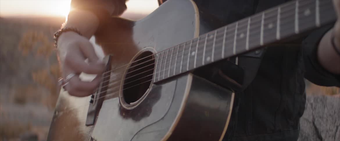 A man plays an acoustic guitar at sunset