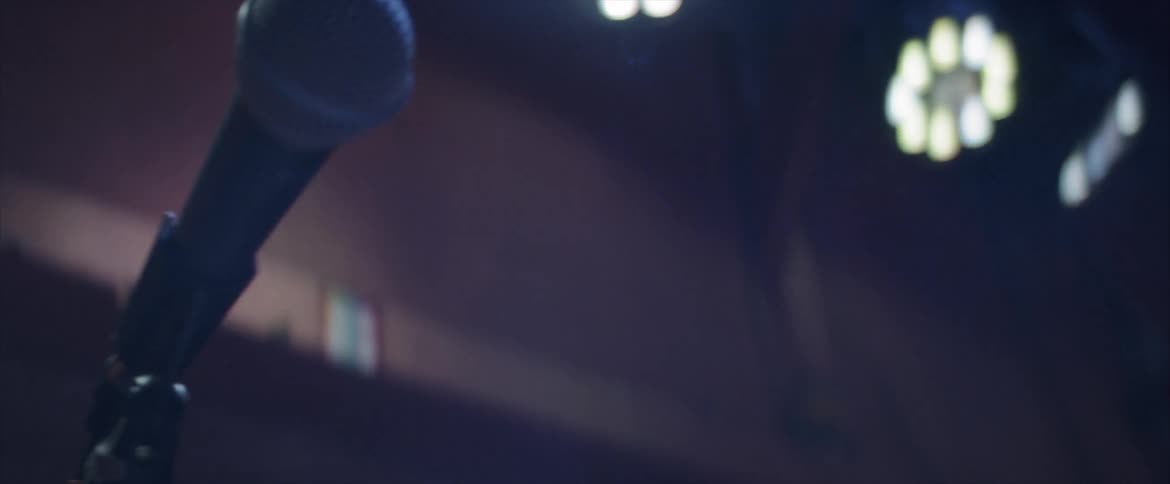 An sm 58 vocal microphone on a stand under stage lights