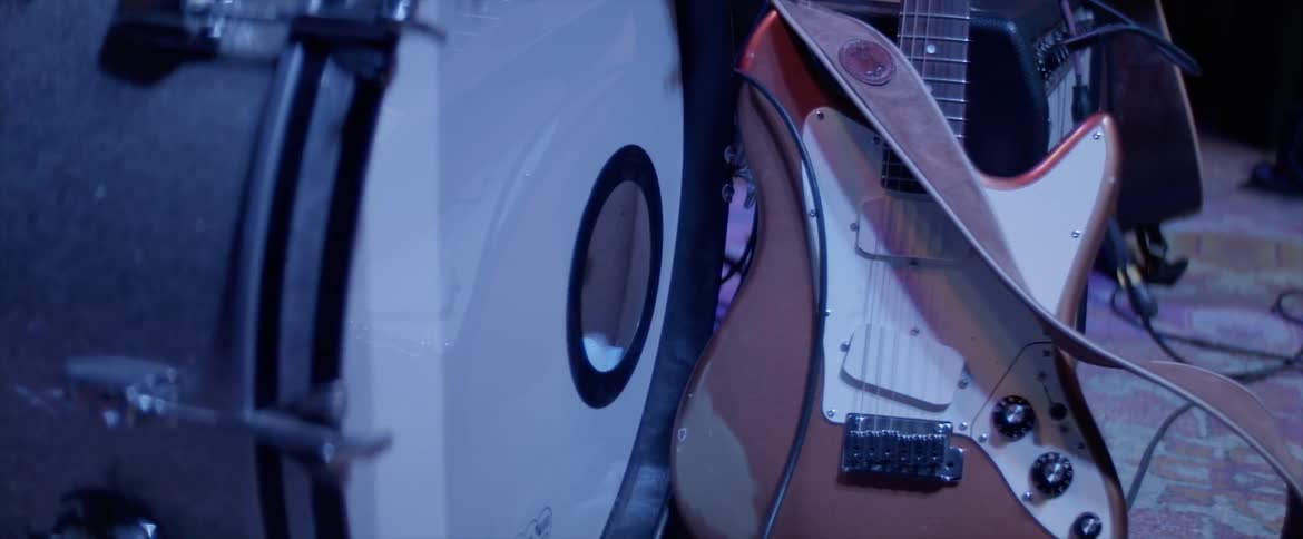 A guitar stands next to the drums