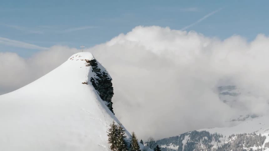 A cross sits atop a snow covered rocky mountain peak