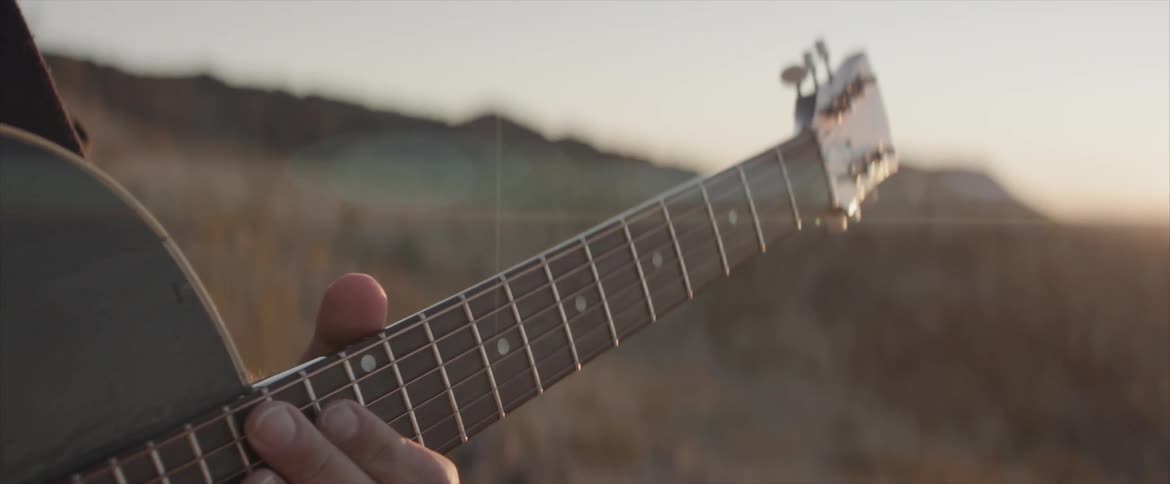 A man holds his guitar ready to play outside at sunset
