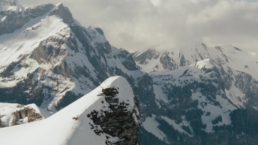 A cross is planted at the top point of a snowy mountain cliff