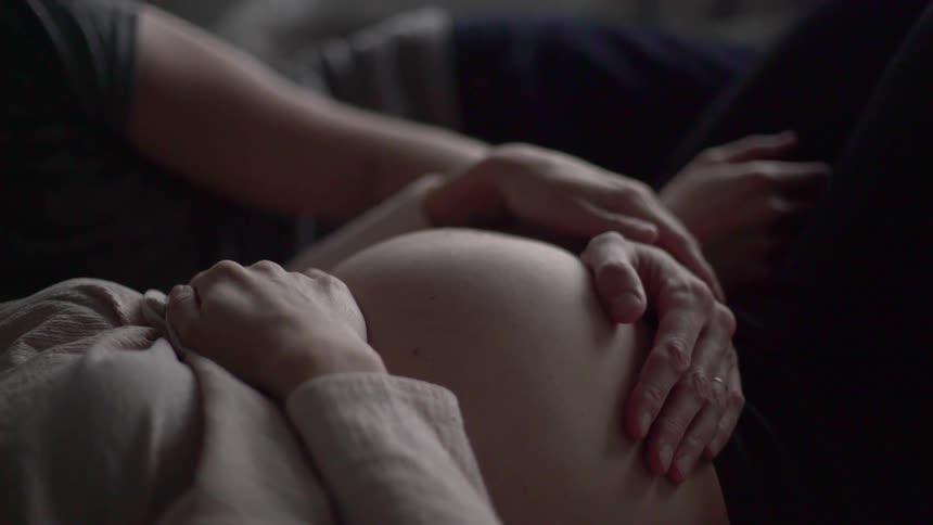 A man lying beside a pregnant woman and touching her stomach