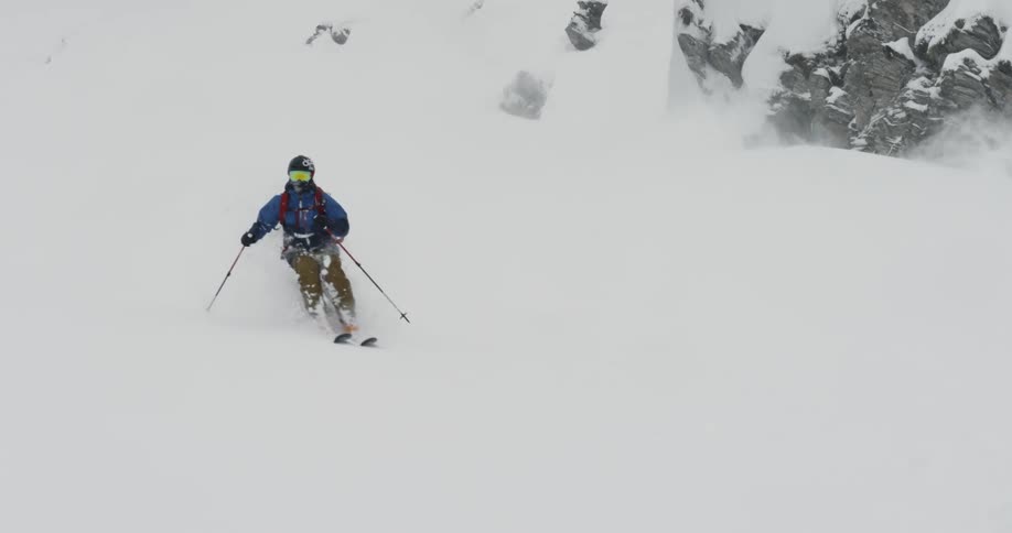 A person skis performing parallel turns on fresh snow while wearing goggles and using poles