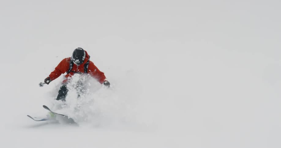 A skier bursts through a snow drift on the way down a run
