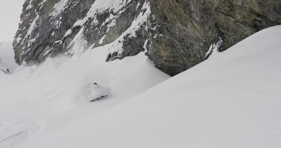 A skier scoots down a steep snowy mountainside