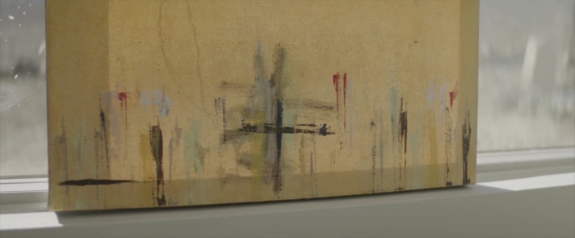 An abstract painting leans against a window on a sunny day