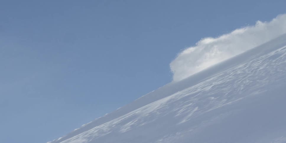 A skier skis down a steep slope through fresh powder on a sunny day
