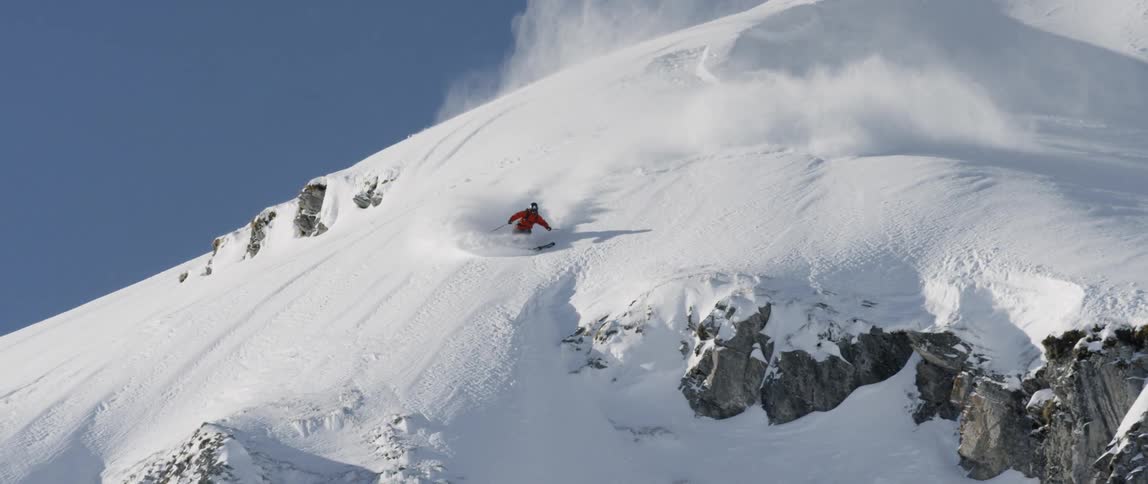 A skier goes down a steep slope as snow flies behind
