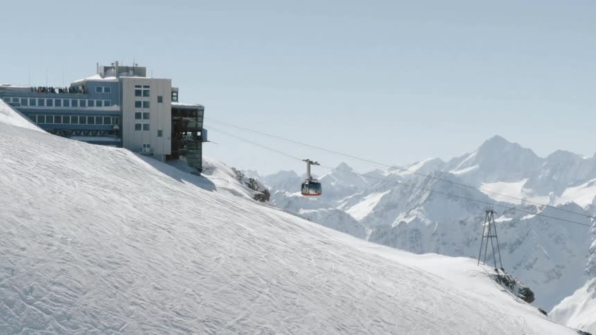 The ski lift travels up the snowy mountain under a blue sky