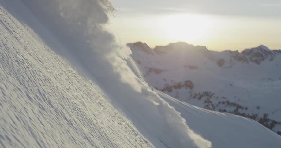 A person skis down a slope kicking up a cloud of snow behind them