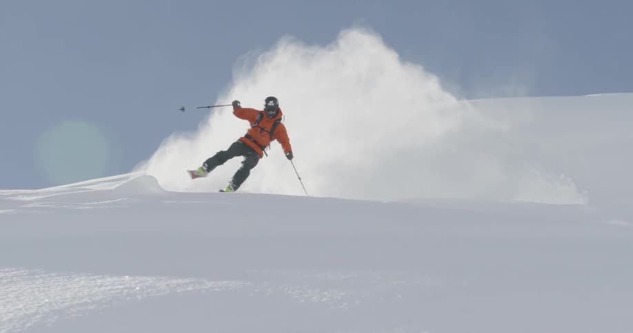 A man skis down a snowy hill under a blue sky