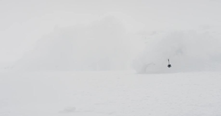 A person in winter gear and goggles is skiing down a slope and spraying snow in the air