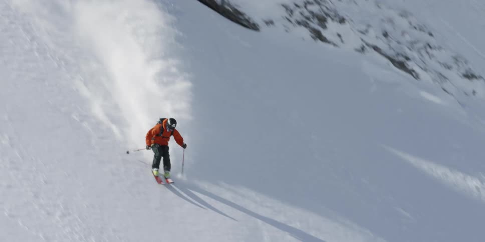 A skier wearing a backpack weaves back and forth while skiing down a mountain covered in fresh snow