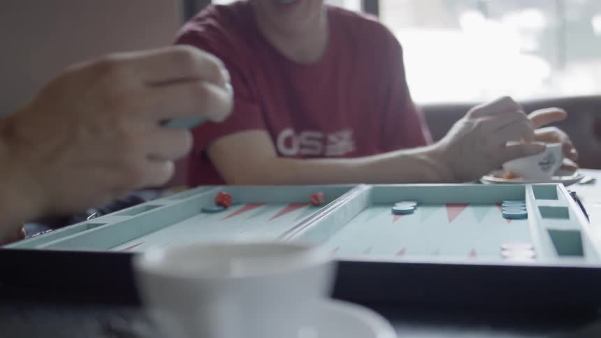 Two men play play backgammon in a caf during daylight