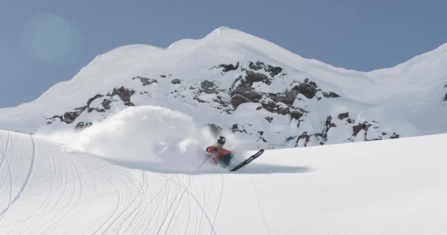 A skier kicks up a huge cloud of snow zipping down the side of a mountain