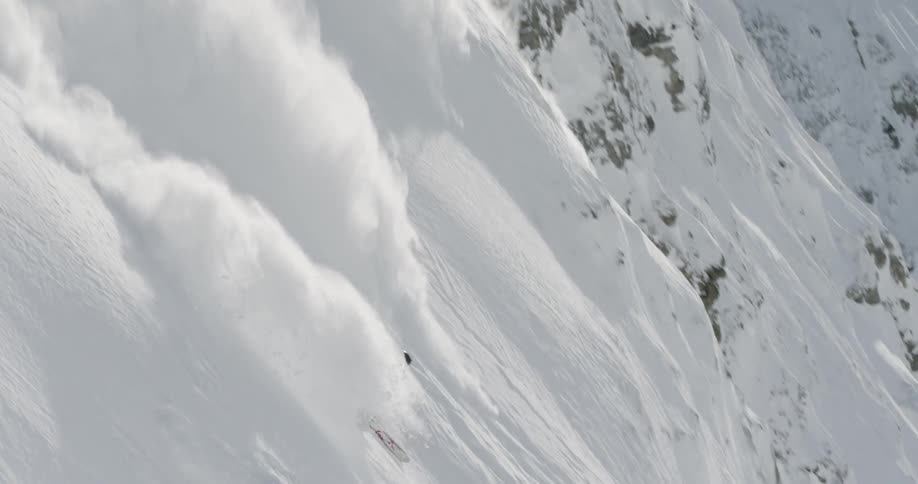A skier skis down a steep rocky slope through fresh powder