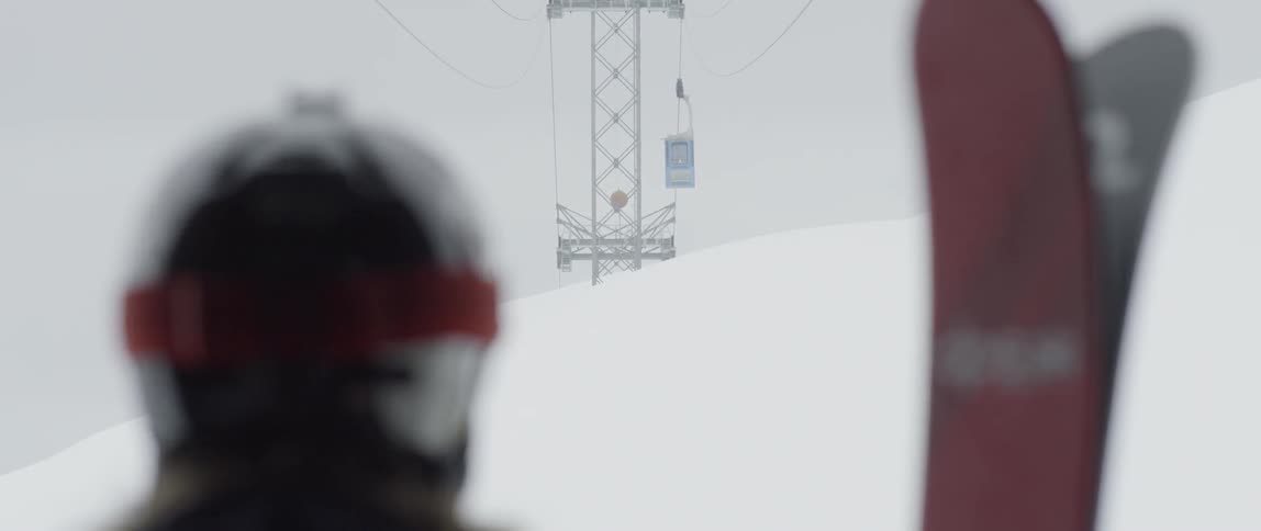 A skier holding a pair of skis while standing below a ski lift