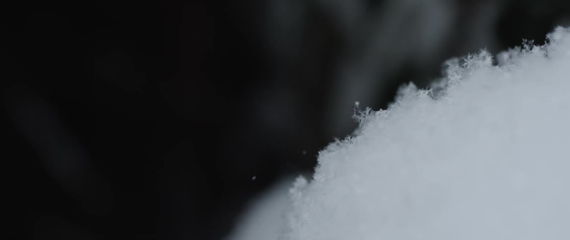 Drops of snow dropping on a pile of snow against a black backdrop