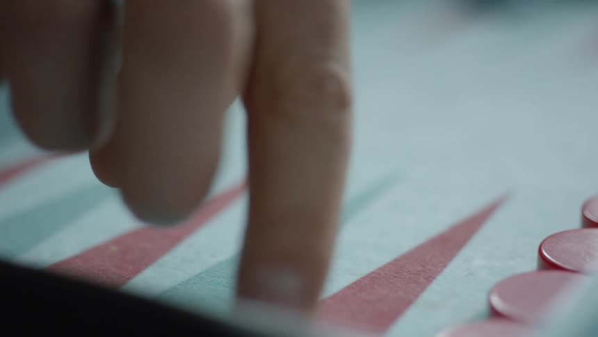 A person is moving a red game piece across the game board while playing backgammon