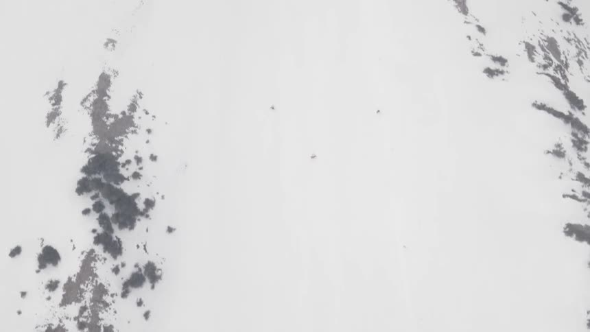 Two skiers ski down a snow covered mountain slope